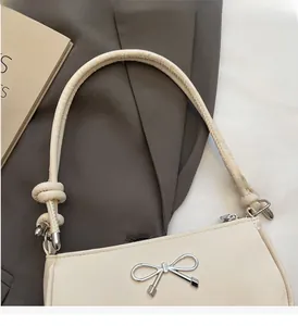 Close-up of beige shoulder bag with silver bow buckle and knotted handle detail