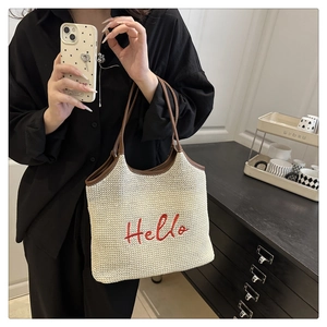 Detail of woven straw tote bag with red Hello embroidery and brown leather handles