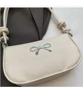Close-up of cream faux leather shoulder bag featuring a silver metal bow and knotted strap
