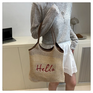 Detail of beige woven tote bag with red Hello embroidery and brown leather straps