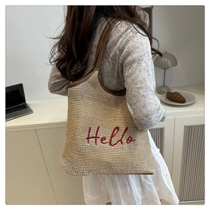 Detail of hand-woven beige tote bag with red Hello embroidery and brown leather handle