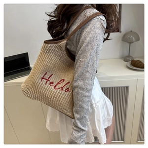 Detail of woven straw tote bag featuring Hello embroidery and brown leather handles