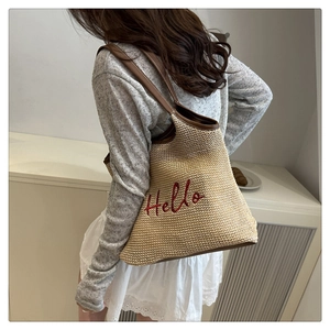 Detail of woven straw tote bag featuring red Hello embroidery and brown leather handle