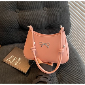 Detail of pink leather handbag featuring a silver metal bow and knotted shoulder strap