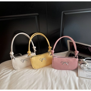 Three macaron-colored crescent bags with woven knots and silver bow details on fabric