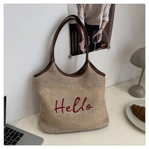 Detail of handwoven straw tote bag with brown leather handles and red Hello embroidery