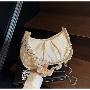 Detail of beige pleated cloud bag with pearl chain and scrunchie handle on wooden stairs