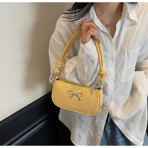 Detail of a bright yellow baguette bag with a silver bow ornament and knotted shoulder strap