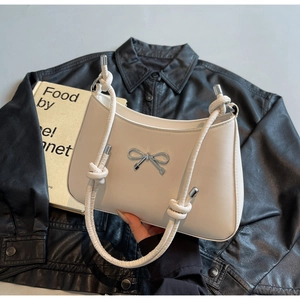 Detailed close-up of cream shoulder bag featuring silver metal bow and knotted strap