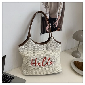 Detail of woven straw tote bag with red Hello embroidery and brown leather handle
