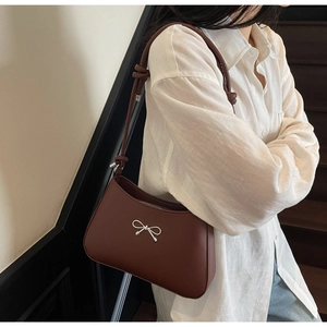 Detail of a brown leather shoulder bag with silver bow accent and knotted strap