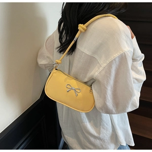 Detail of yellow baguette bag with silver metallic bow and knotted strap on shoulder