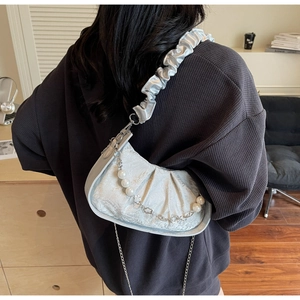 Detail of blue crescent bag with pearl chain and ruffled strap on a model