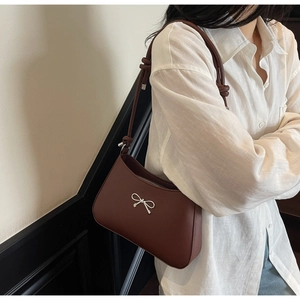 Close-up of brown faux leather shoulder bag featuring a silver bow buckle and knotted strap