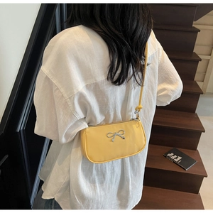 Close-up of bright yellow shoulder bag with silver metallic bow detail and zip closure