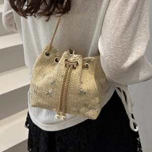 Floral embroidered straw bucket bag with pearl chain strap worn by a model in soft light