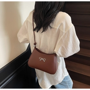 Brown leather underarm bag with silver bow accent and slim strap on a model