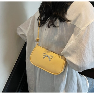 Detail of a yellow French-style crescent bag with a silver bow ornament on the shoulder