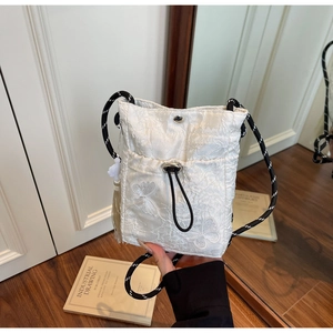 Detail of white lace butterfly embroidery on a drawstring bucket bag with tassel