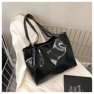 Détail du sac cabas noir brillant avec un nœud argenté et des fixations en anneau