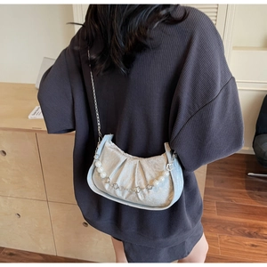 Detail of light blue pleated cloud bag with pearl chain on model in indoor setting
