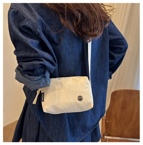 Détail d'un sac bandoulière minimaliste en toile crème avec un badge métallique vintage