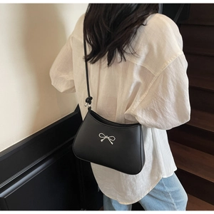 Detail shot of a black minimalist crescent shoulder bag with silver bow accent on model