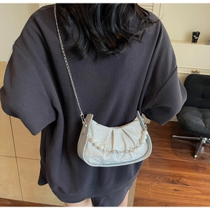 Detail of pleated cloud bag with pearl chain strap worn over a grey knit sweater