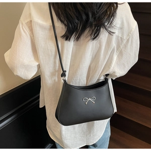 Detail of minimalist black leather shoulder bag featuring a silver metal bow accent