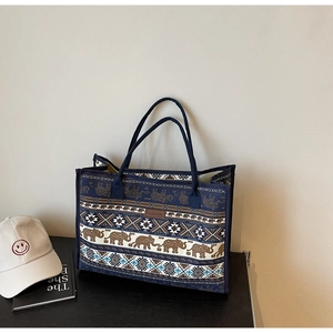 Detail of blue canvas tote bag with ethnic elephant patterns and brown leather logo