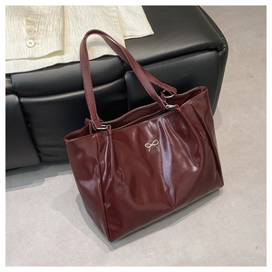 Close-up of deep red glossy tote bag with silver bow detail on black leather seat