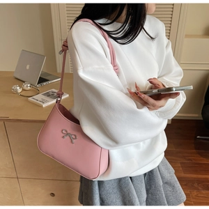 Pink leather shoulder bag with silver metal bow detail shown on model in home setting
