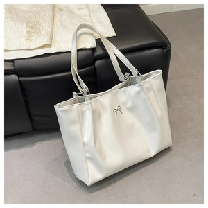 Detailed close-up of a cream-colored tote bag with a silver metallic bow decoration