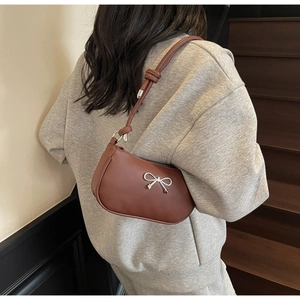 Detail of a brown leather crescent bag featuring a silver metal bow accent and slim strap