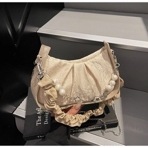 Detailed view of beige pleated cloud bag with pearl strap on a designer book