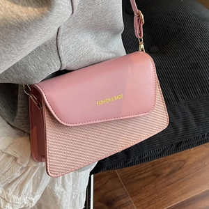 Light pink crossbody bag with woven texture and gold lettering on a stylish wide strap