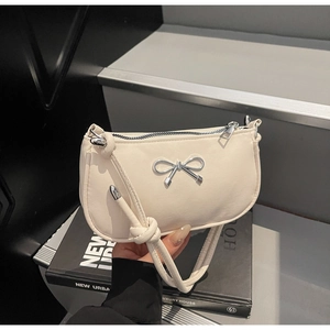 Detail of silver bow hardware and knotted shoulder strap on cream-colored crescent bag