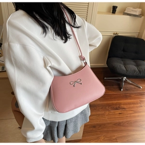 Pink faux leather shoulder bag with silver bow accent shown in a lifestyle setting