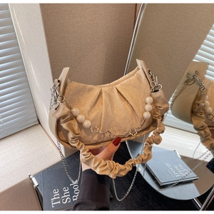 Detail of beige pleated cloud bag featuring pearl chain and floral metal charms