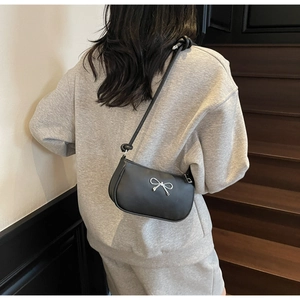 Detailed view of black minimalist shoulder bag with silver bow accent and knotted straps