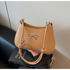 Detail of beige shoulder bag featuring a knotted handle and silver bow embellishment