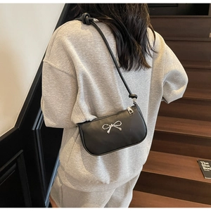 Close-up of black matte leather shoulder bag featuring a silver bow buckle and knotted strap