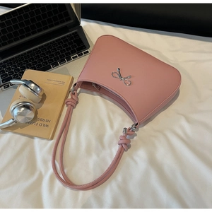 Detail of pink half-moon shoulder bag with silver bow accent and knotted strap on white linen