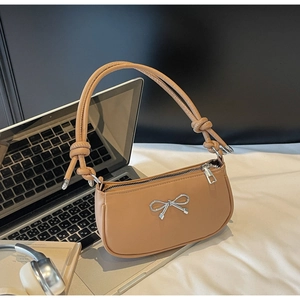 Detail of light brown crescent shoulder bag with silver bow accent on a white desk