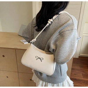 Detail of white underarm bag with silver bow accent and knotted strap on model shoulder