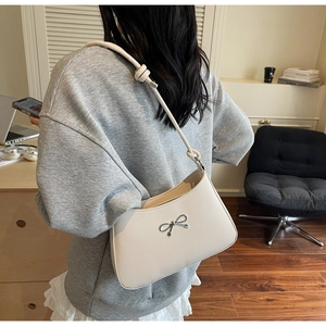 Creamy white underarm bag with silver bow detail and knotted strap shown on model