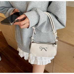 Detailed view of cream crescent shoulder bag with silver bow accent and knotted strap