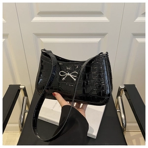 Détail d'un sac à bandoulière noir vernis motif crocodile avec nœud argenté