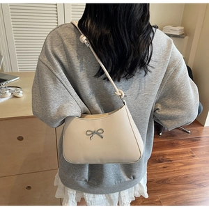Detailed back view of a cream leather shoulder bag featuring a silver metal bow buckle