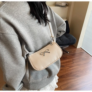 Detail view of cream crescent shoulder bag with silver metal bow and slim strap